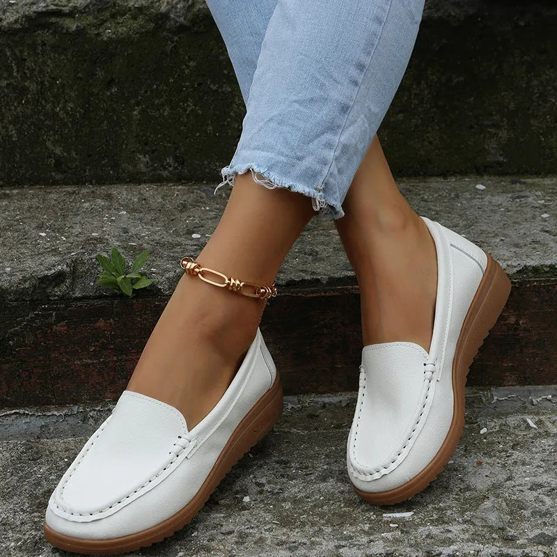Women's flat slip-on loafers in PU leather, showing colour options and round toe design with decorative stitching.