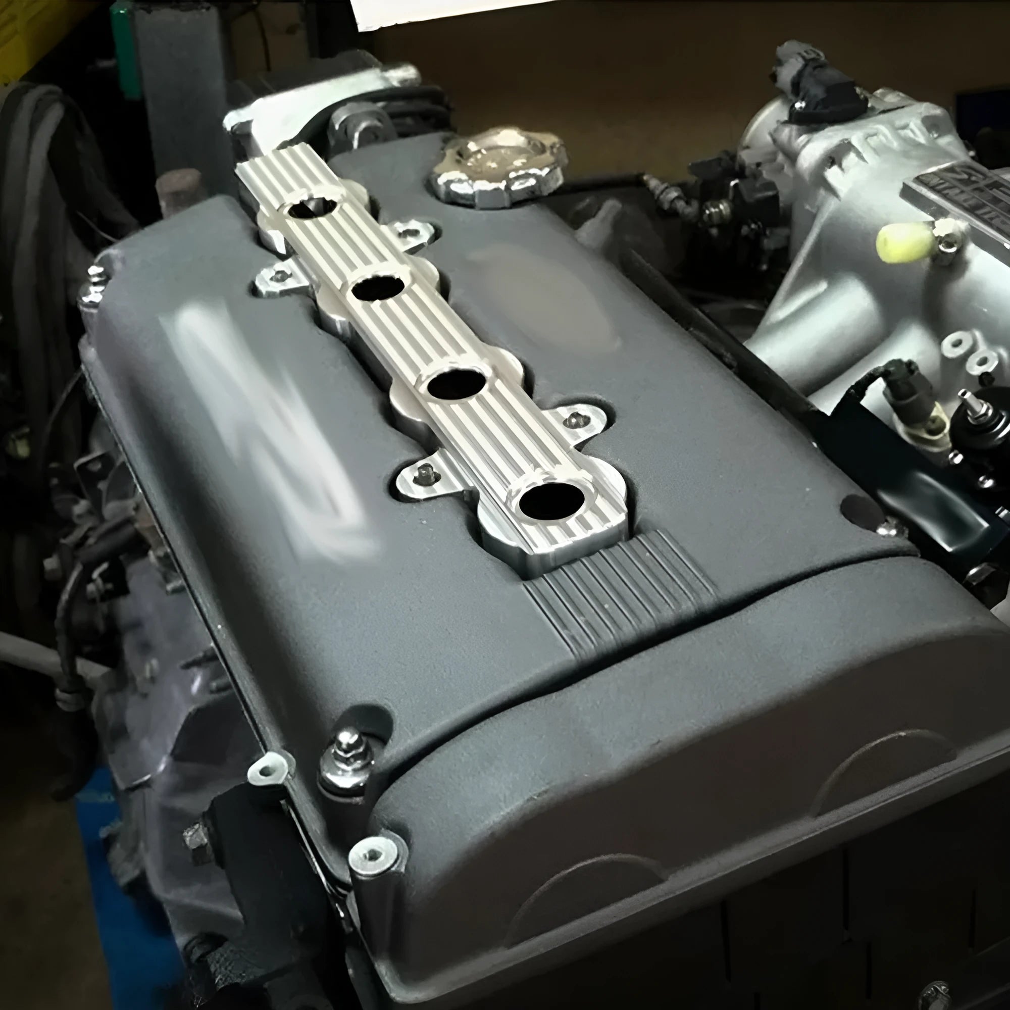 Aluminium alloy engine harness housing bracket in blue, red, and silver, showing versions with and without mounting holes.