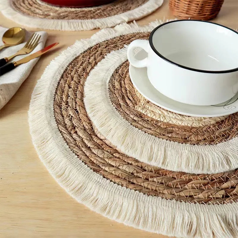 Round natural papyrus straw placemat with tassel edge on a wooden table.