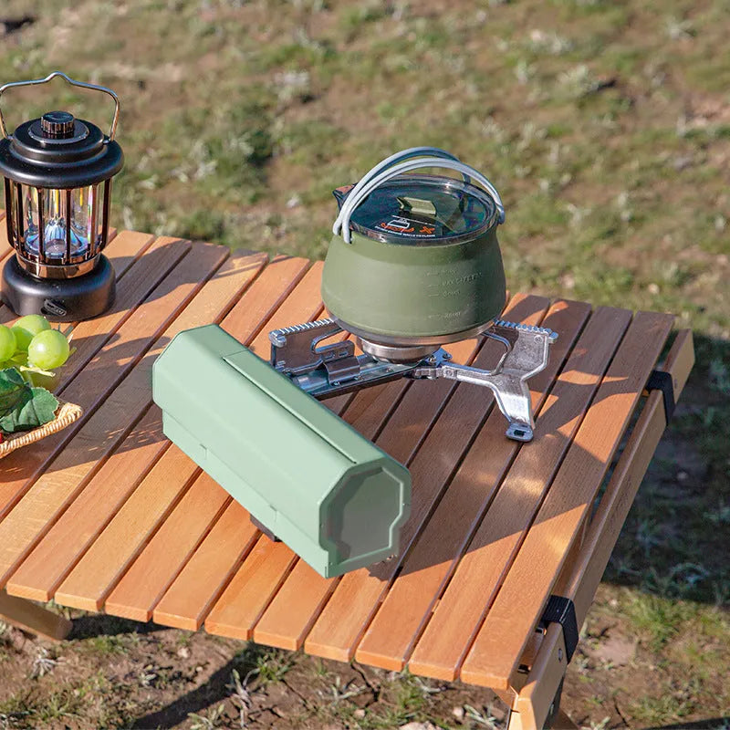 Green portable folding camping gas stove with adjustable valve on a serrated bracket, shown with its storage bag.