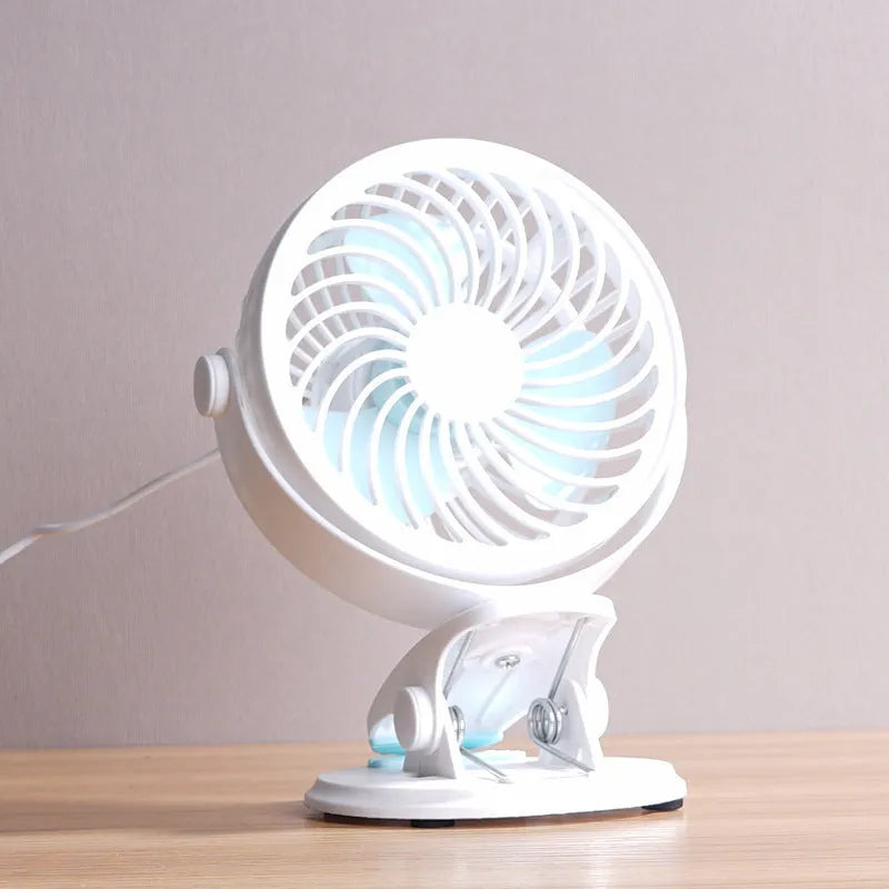 Small white USB desktop fan with clip attached to a desk edge, showing three blades.