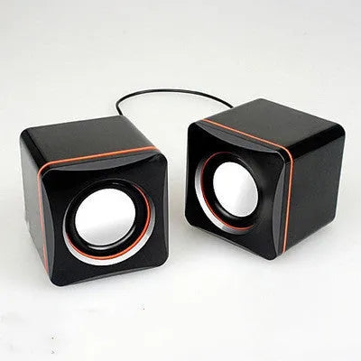 Small black square USB-powered 2.0 computer speaker on a desk next to a laptop