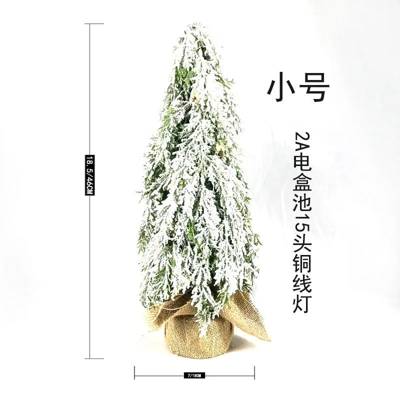Small 24-inch white artificial Christmas tree with built-in LED lights and simulated snow sprayer on a desktop.