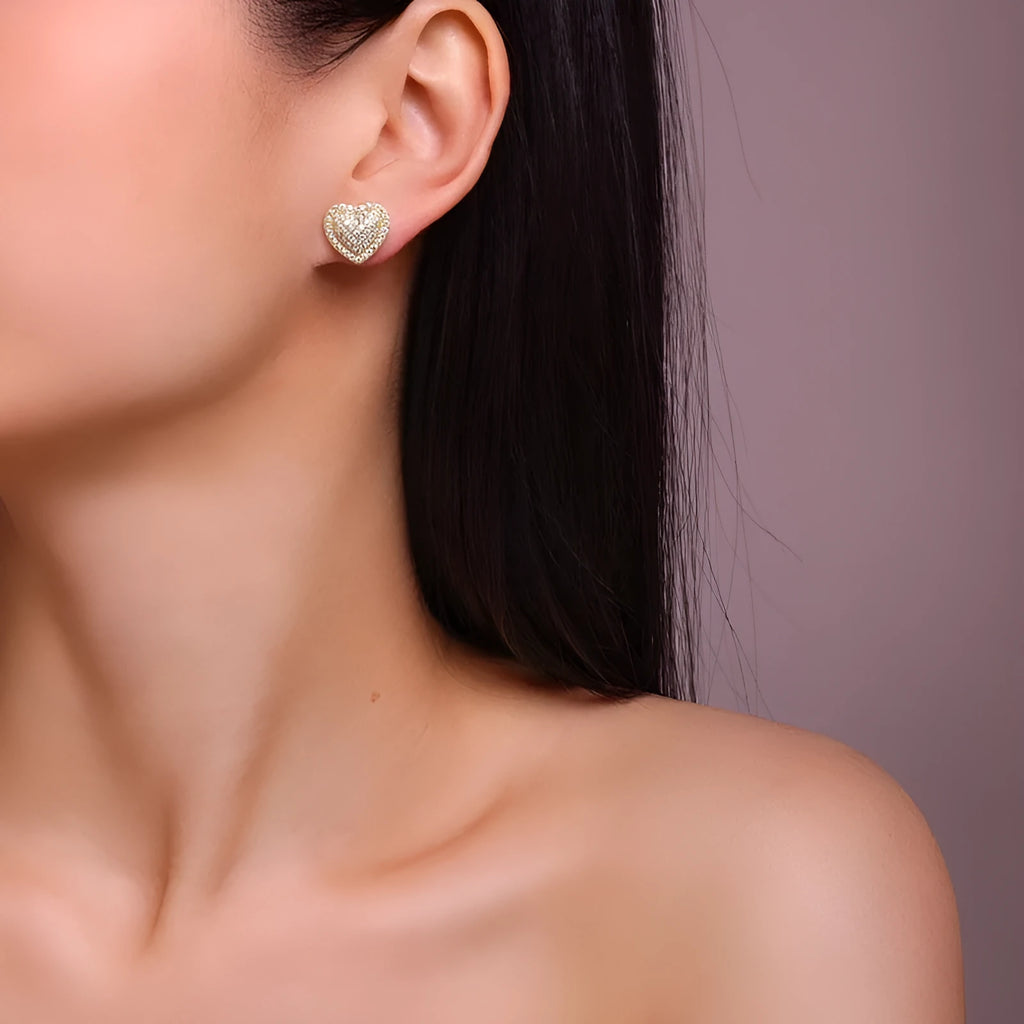 A pair of gold-coloured heart-shaped moissanite stud earrings on a plain background.