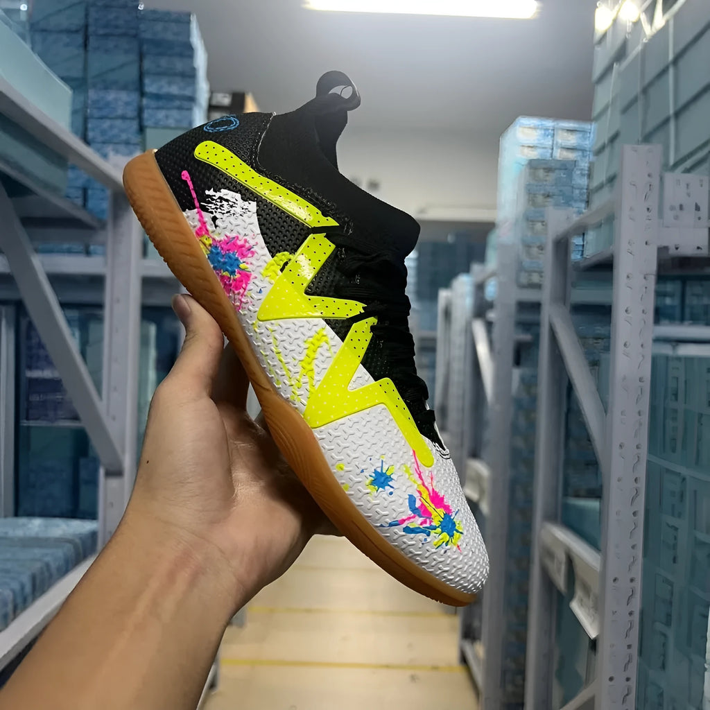 Low-top soccer boots in black and yellow colourway with spiked rubber sole, shown on a firm ground surface.