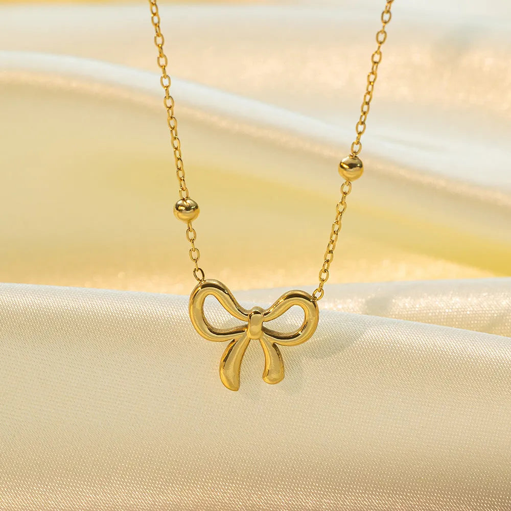 Gold coloured titanium steel necklace with a bow charm on a cross chain.