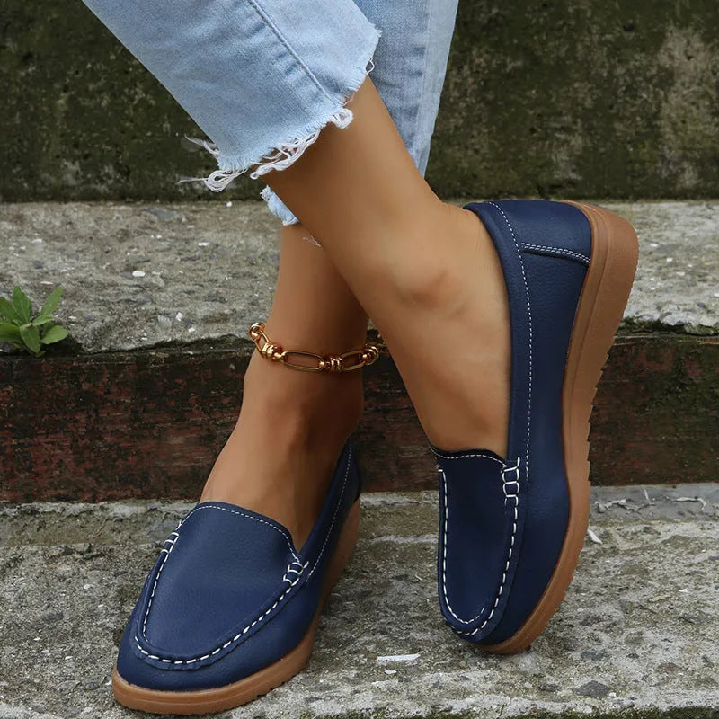 Women's flat slip-on loafers in PU leather, showing colour options and round toe design with decorative stitching.