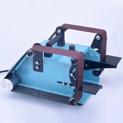 Blue desktop dual-axis belt sander with variable speed control and included knife sharpening tool on a workbench.