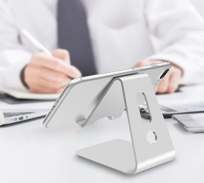Aluminium alloy universal phone and tablet stand in silver colour on a wooden desk.