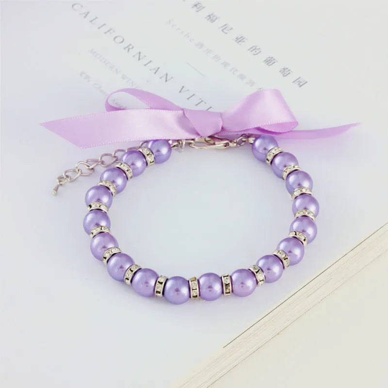 Small dog wearing adjustable pearl necklace with rhinestones and ribbon bow decorative collar