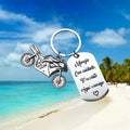 Close-up of a metal motorcycle-themed inspirational keychain next to a red flannel storage bag