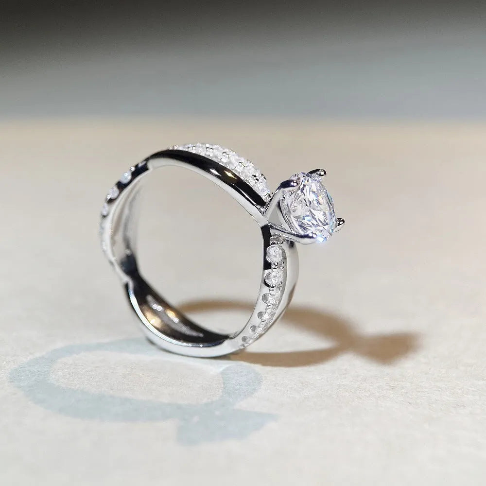 Women's silver ring with a 1 karat moissanite stone in a four-claw twisted arm setting, showing a geometric cross design.