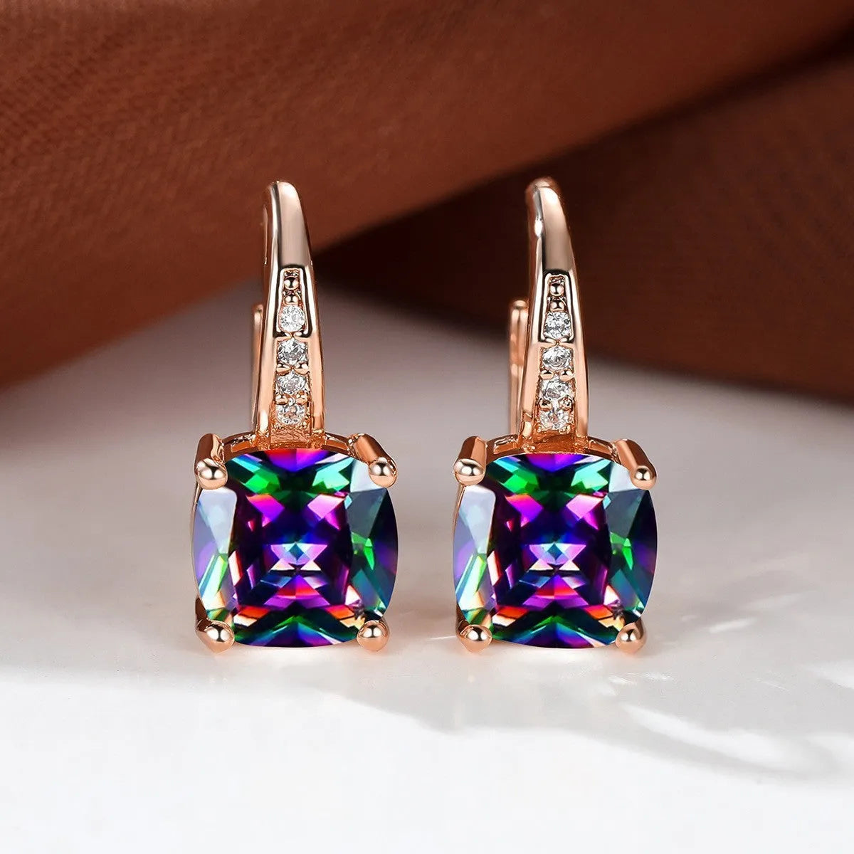 Geometric copper ear hook with round element and inlaid square zircon stone, shown in a golden colour.