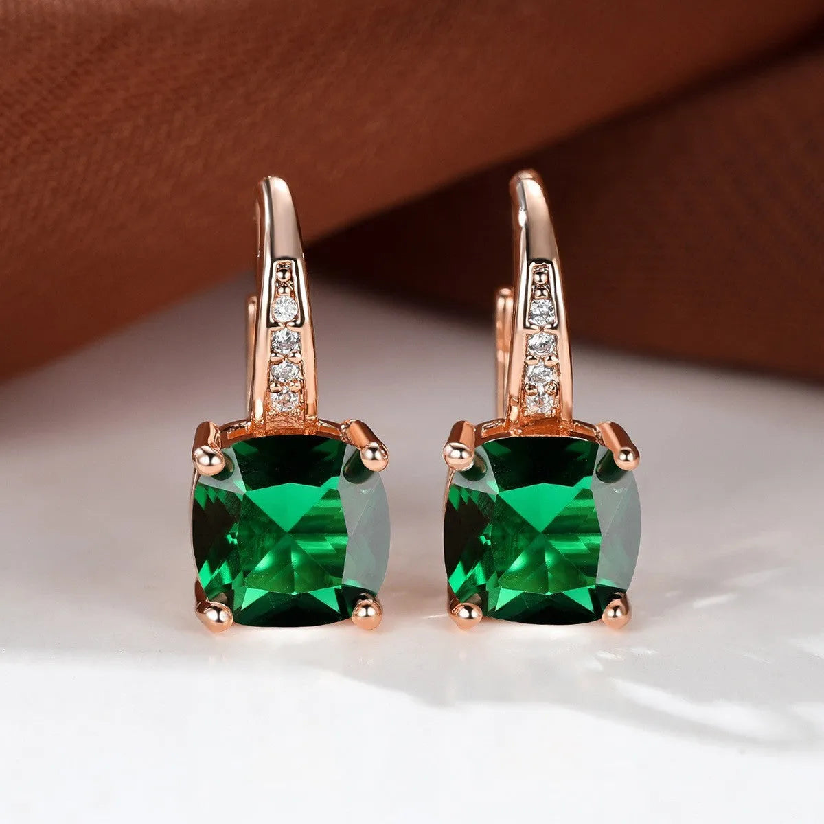 Geometric copper ear hook with round element and inlaid square zircon stone, shown in a golden colour.