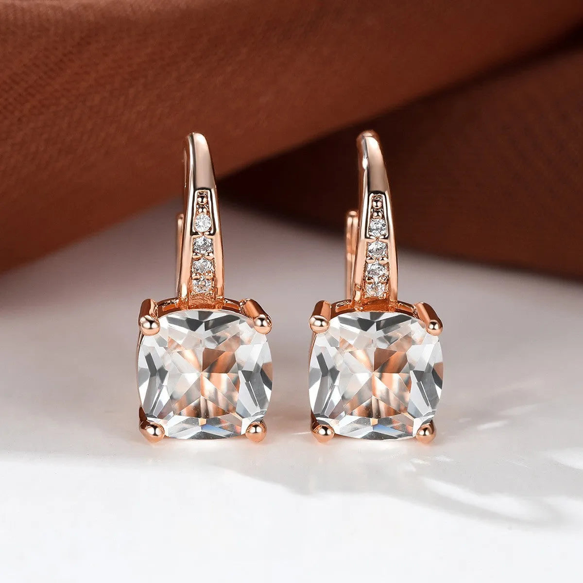 Geometric copper ear hook with round element and inlaid square zircon stone, shown in a golden colour.