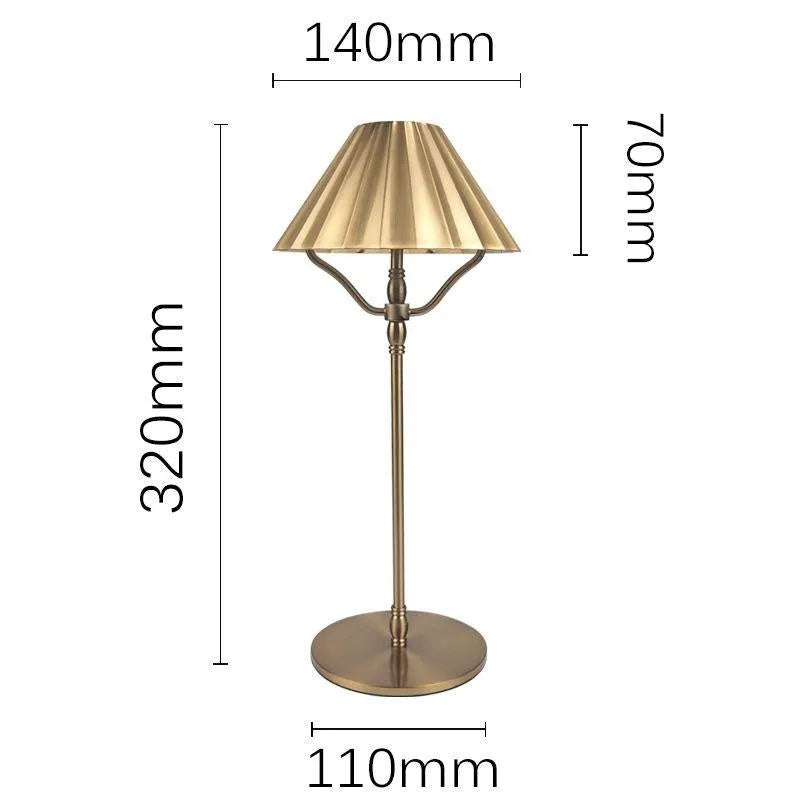 Gold alloy desk lamp with a cylindrical shade, shown lit with warm white light on a wooden desk.