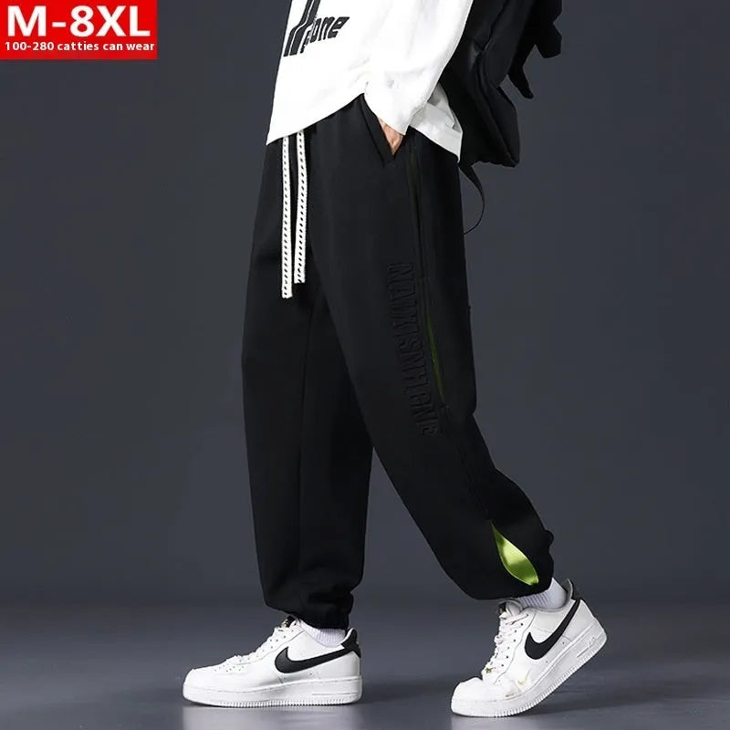 Man wearing grey green loose-fit cotton trousers with elastic ankle bands and visible stitch detailing.