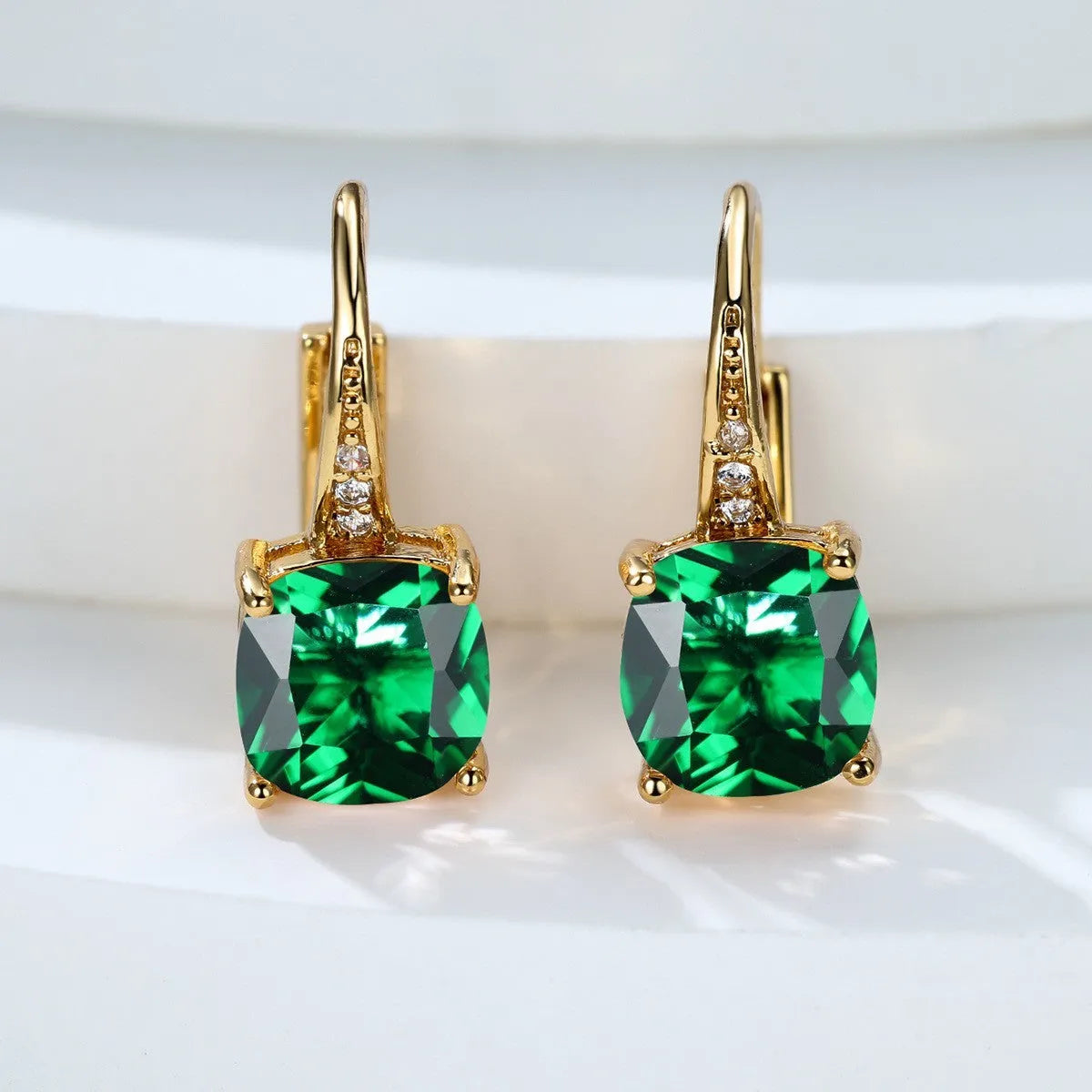 Geometric copper ear hook with round element and inlaid square zircon stone, shown in a golden colour.