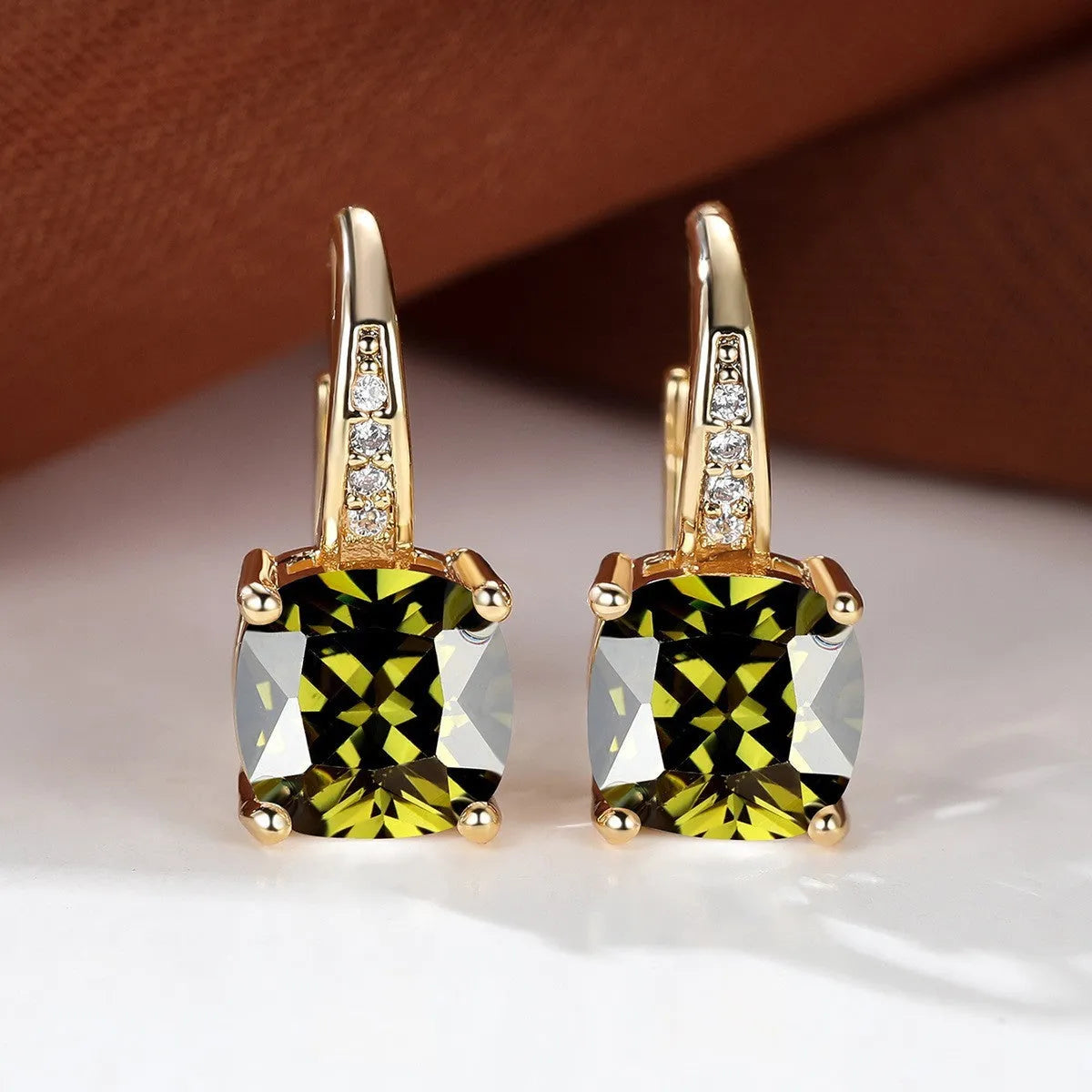 Geometric copper ear hook with round element and inlaid square zircon stone, shown in a golden colour.