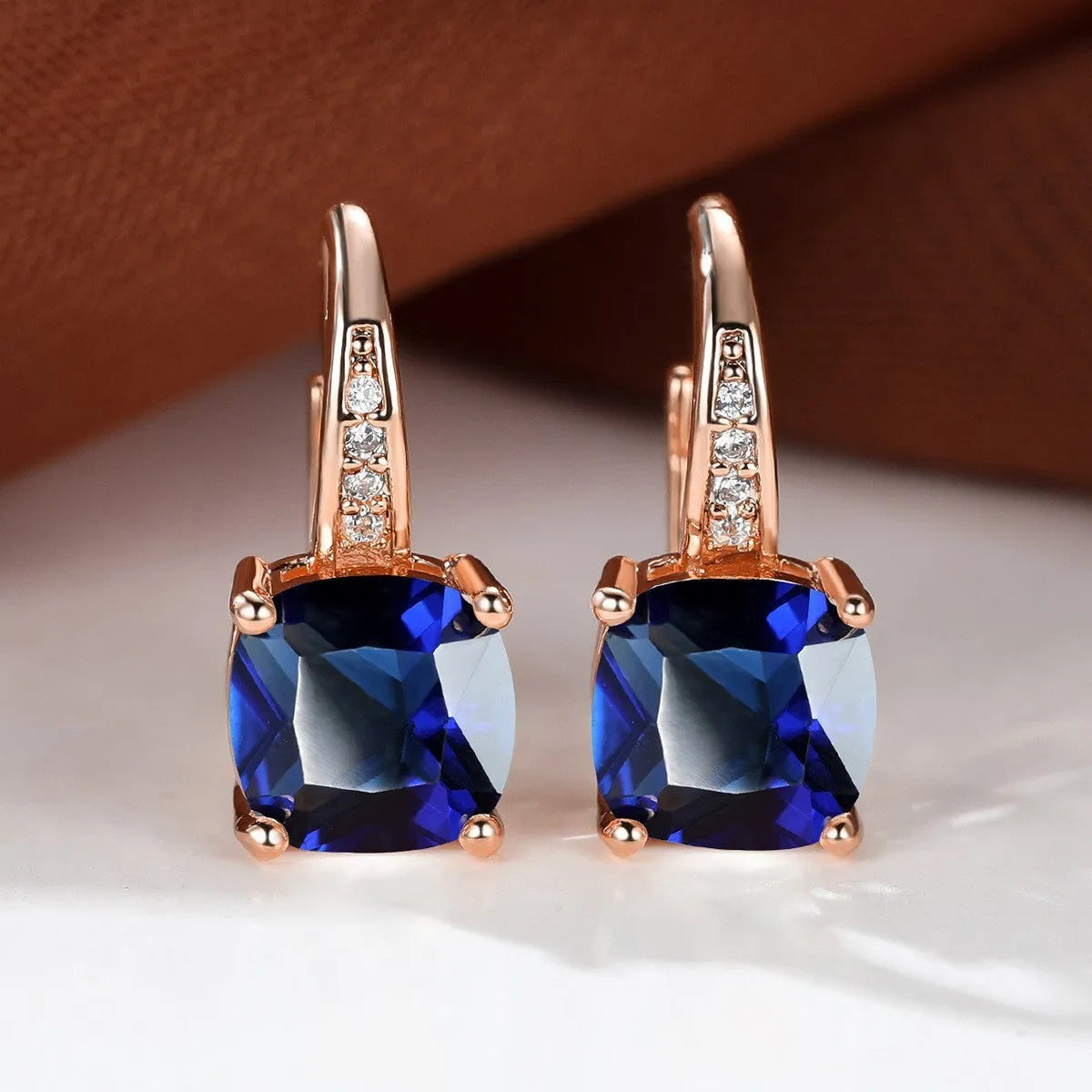 Geometric copper ear hook with round element and inlaid square zircon stone, shown in a golden colour.