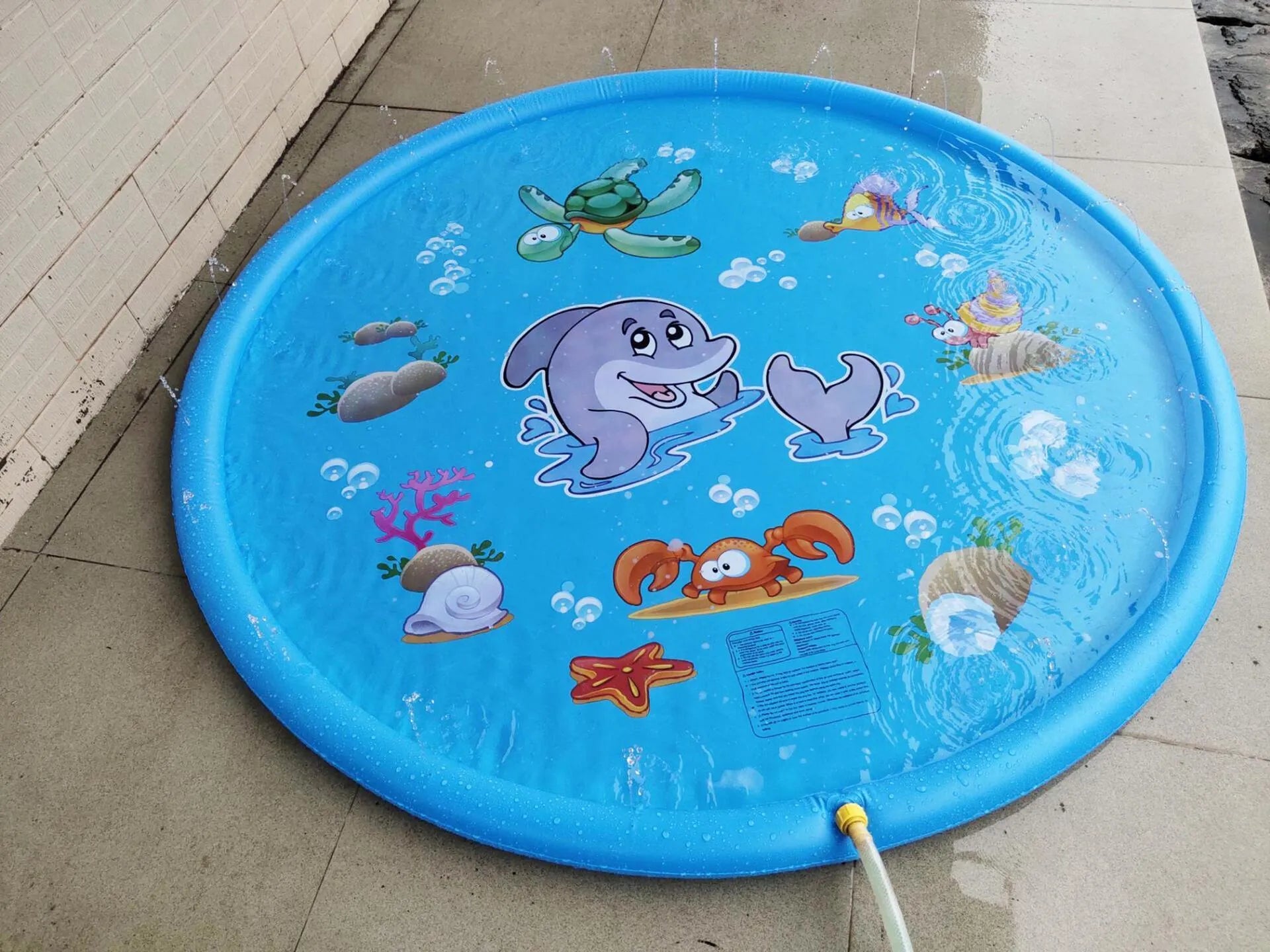 Blue PVC children's water spray play mat with marine animal designs laid out on grass.