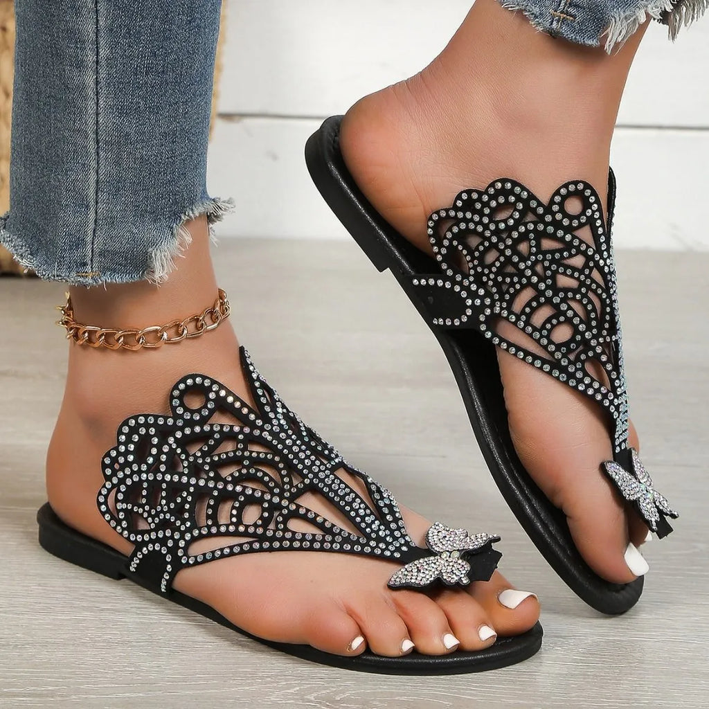 Women's black flip-toe sandals with rhinestone details on the hollow-out PU upper and a flat rubber sole.