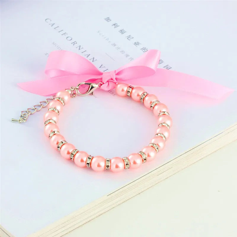 Small dog wearing adjustable pearl necklace with rhinestones and ribbon bow decorative collar