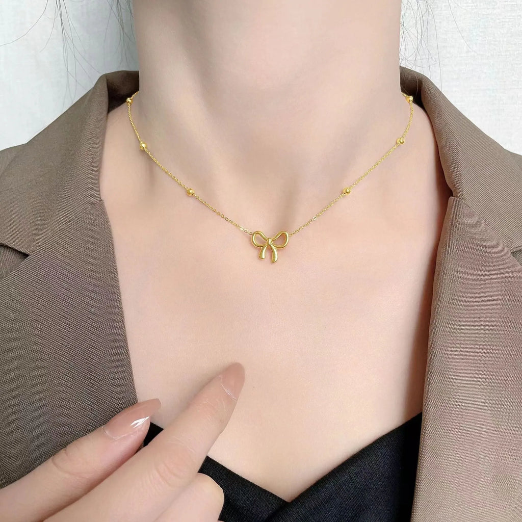 Gold coloured titanium steel necklace with a bow charm on a cross chain.