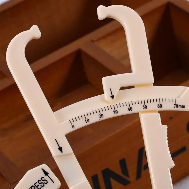 Clear acrylic body fat caliper skin fold thickness meter showing measurement scale