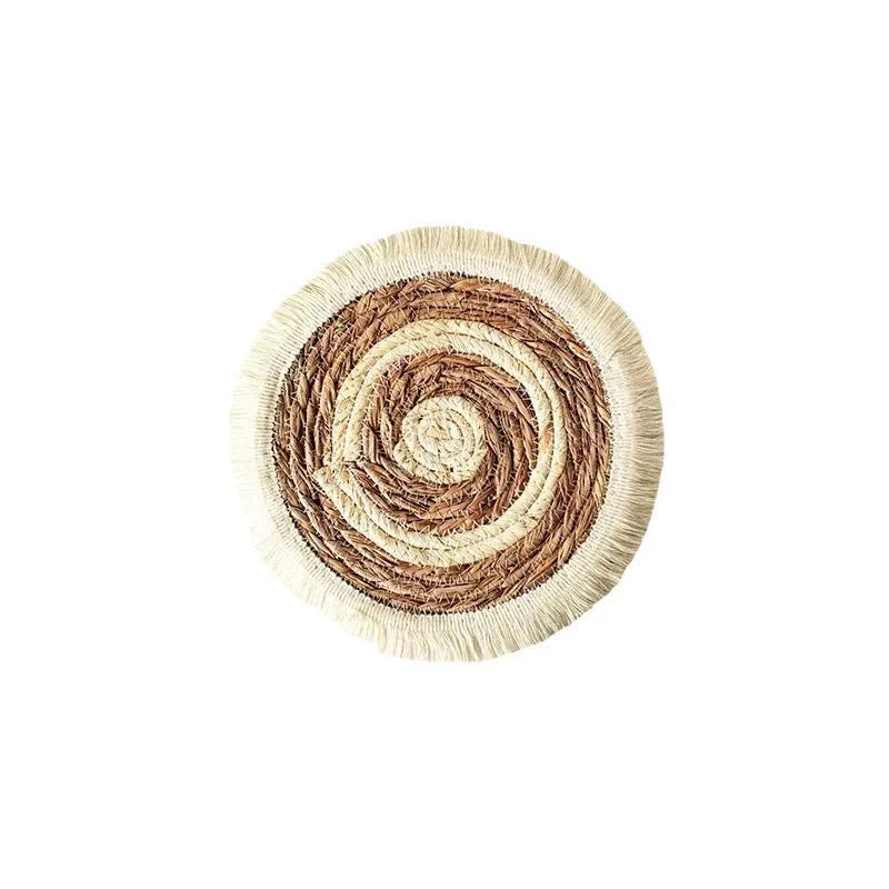 Round natural papyrus straw placemat with tassel edge on a wooden table.