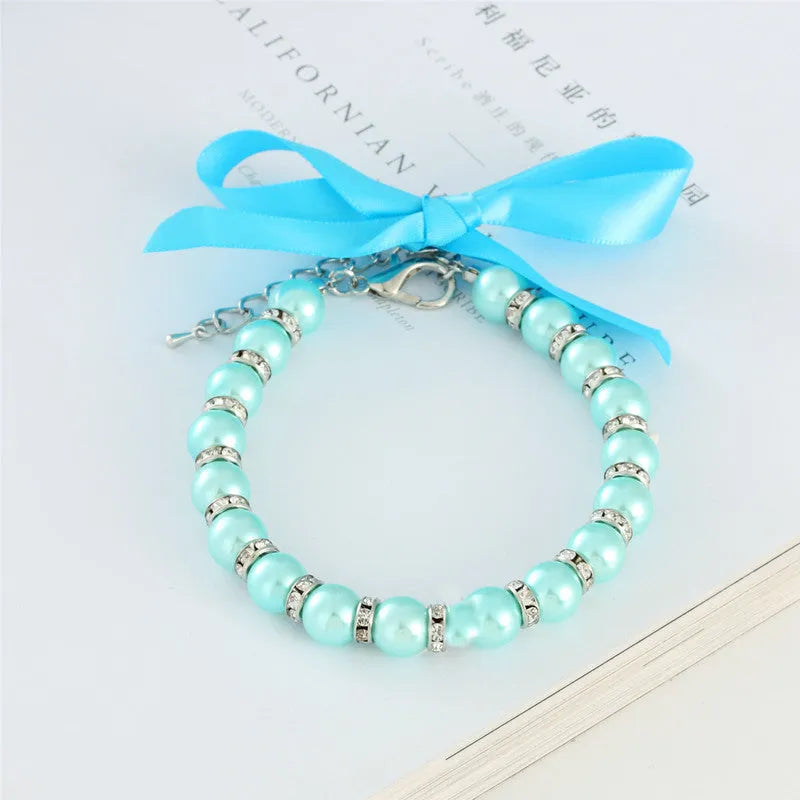 Small dog wearing adjustable pearl necklace with rhinestones and ribbon bow decorative collar