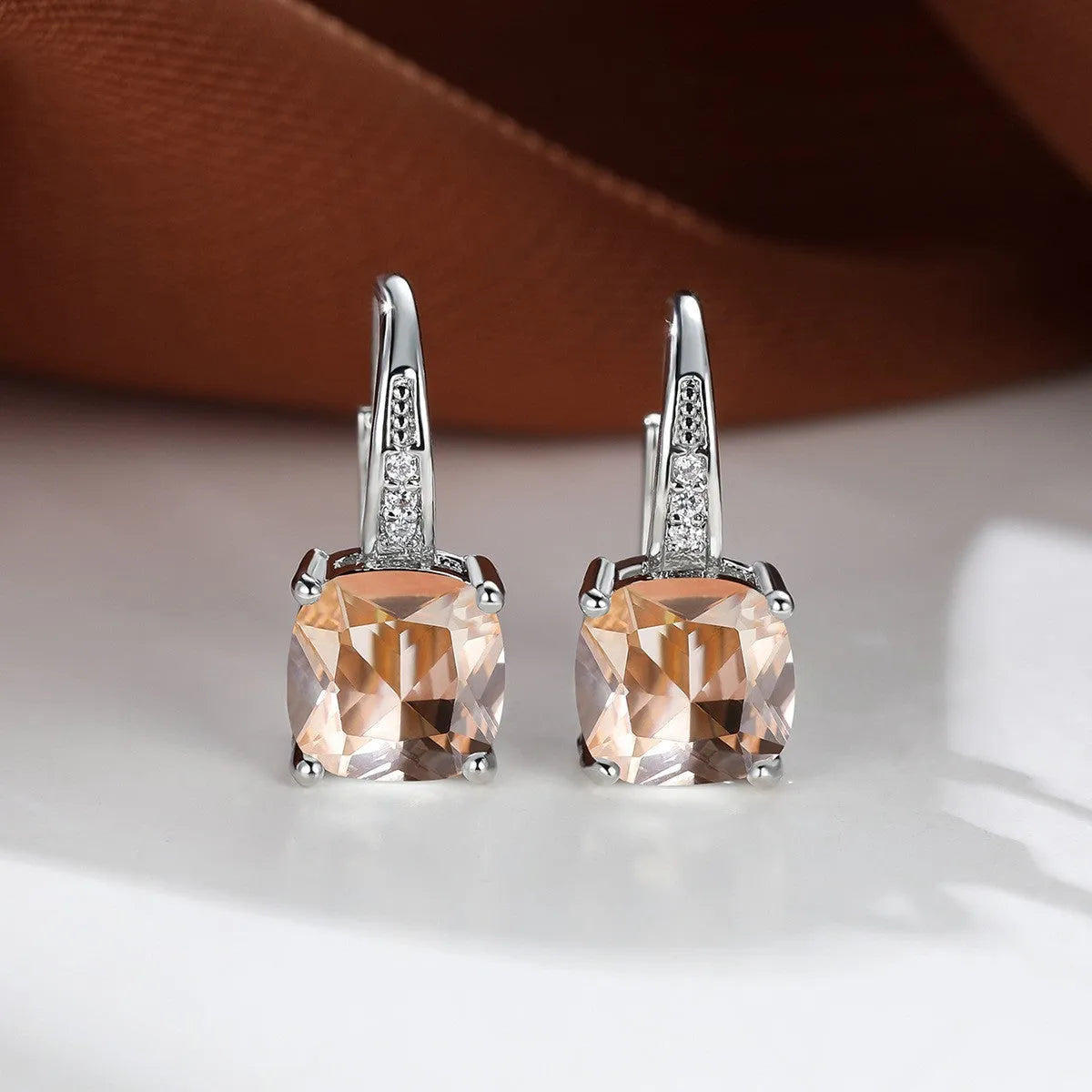 Geometric copper ear hook with round element and inlaid square zircon stone, shown in a golden colour.