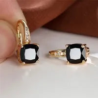Geometric copper ear hook with round element and inlaid square zircon stone, shown in a golden colour.