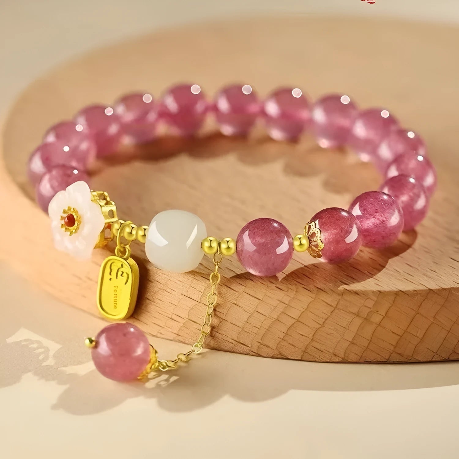 Handmade strawberry quartz crystal bracelet with Hetian jade peach blossom charm on a wrist.
