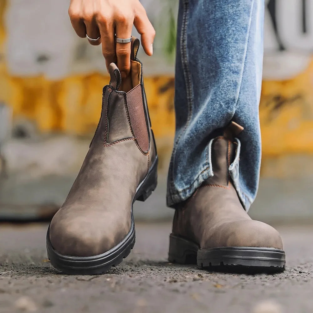 Vintage brown frosted finish Chelsea boots with car suture detailing on a wooden floor.
