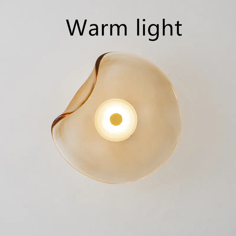 Round glass wall lamp in cognac colour mounted beside a bed with warm light illumination