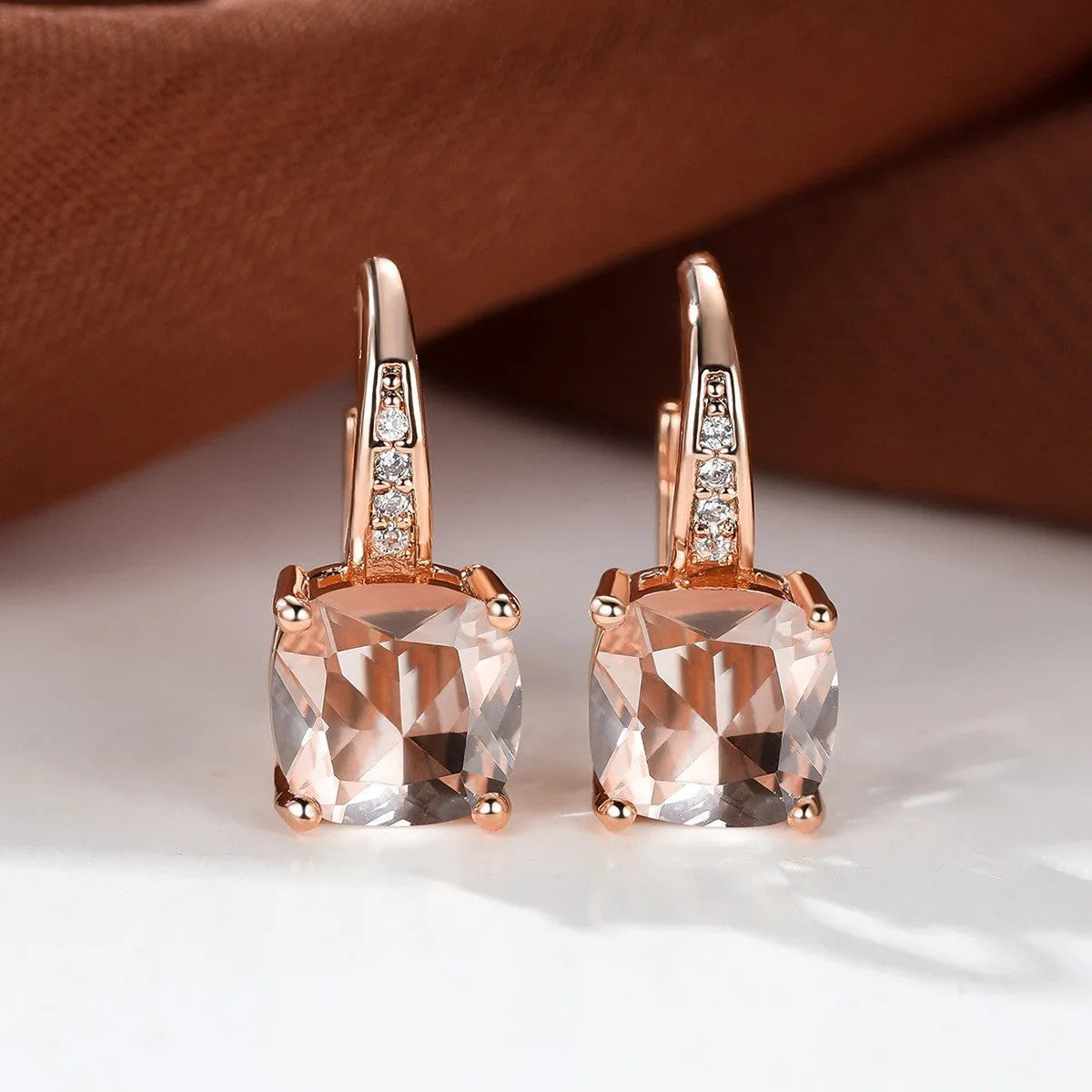 Geometric copper ear hook with round element and inlaid square zircon stone, shown in a golden colour.