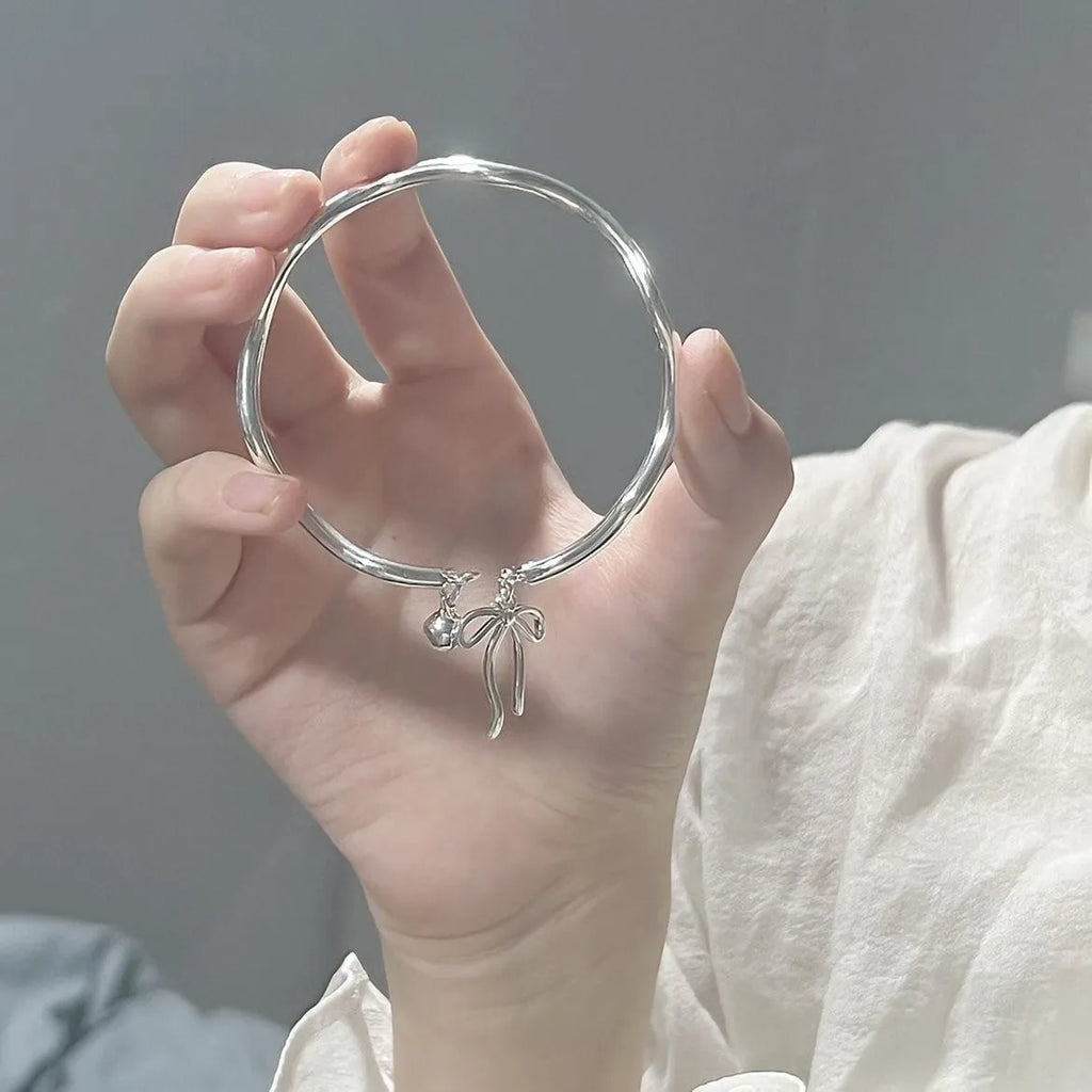 Silver adjustable bracelet with bow charm featuring bell opening detail