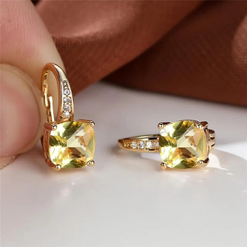 Geometric copper ear hook with round element and inlaid square zircon stone, shown in a golden colour.