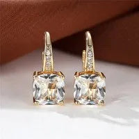 Geometric copper ear hook with round element and inlaid square zircon stone, shown in a golden colour.