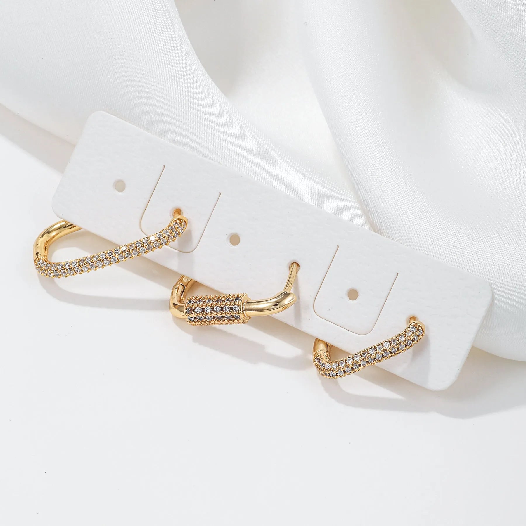 Geometric ear clips set with micro inlaid zircon detailing on copper, showing ellipse and quadrilateral shapes in gold and white finishes