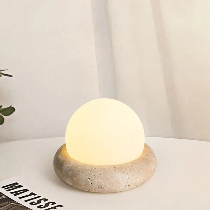 Cream-coloured round bedside night lamp with remote control on wooden table