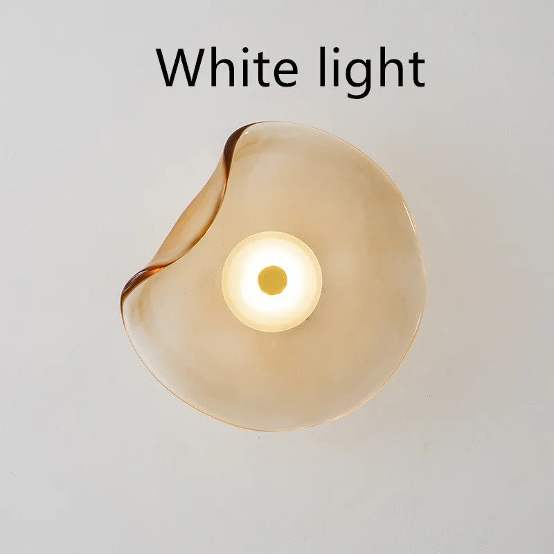 Round glass wall lamp in cognac colour mounted beside a bed with warm light illumination