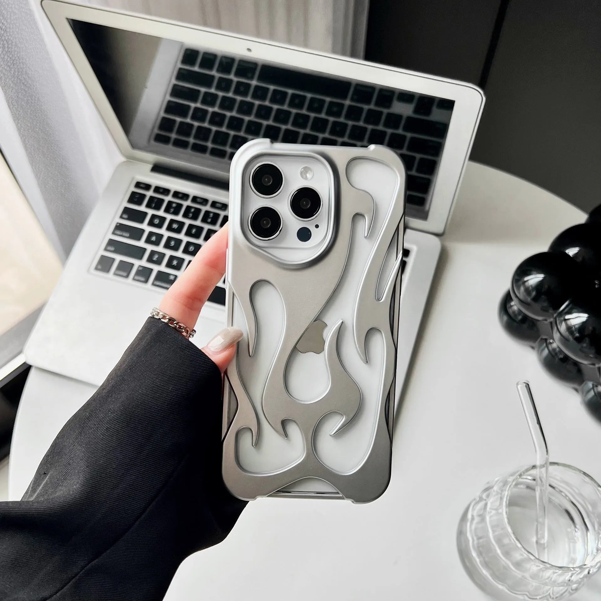 Apple iPhone case with hollow flame pattern and electroplated finish in silver, shown on a phone.