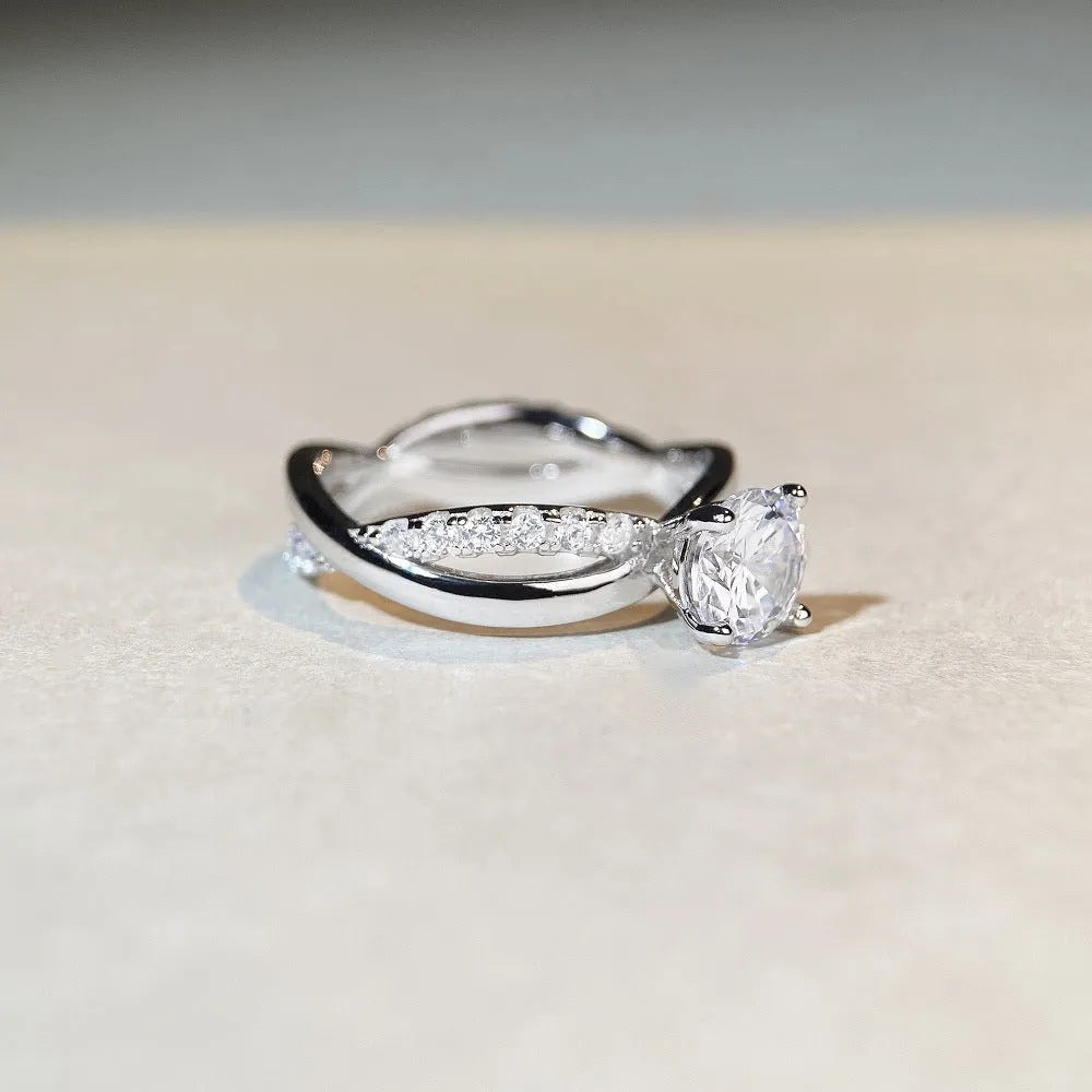 Women's silver ring with a 1 karat moissanite stone in a four-claw twisted arm setting, showing a geometric cross design.