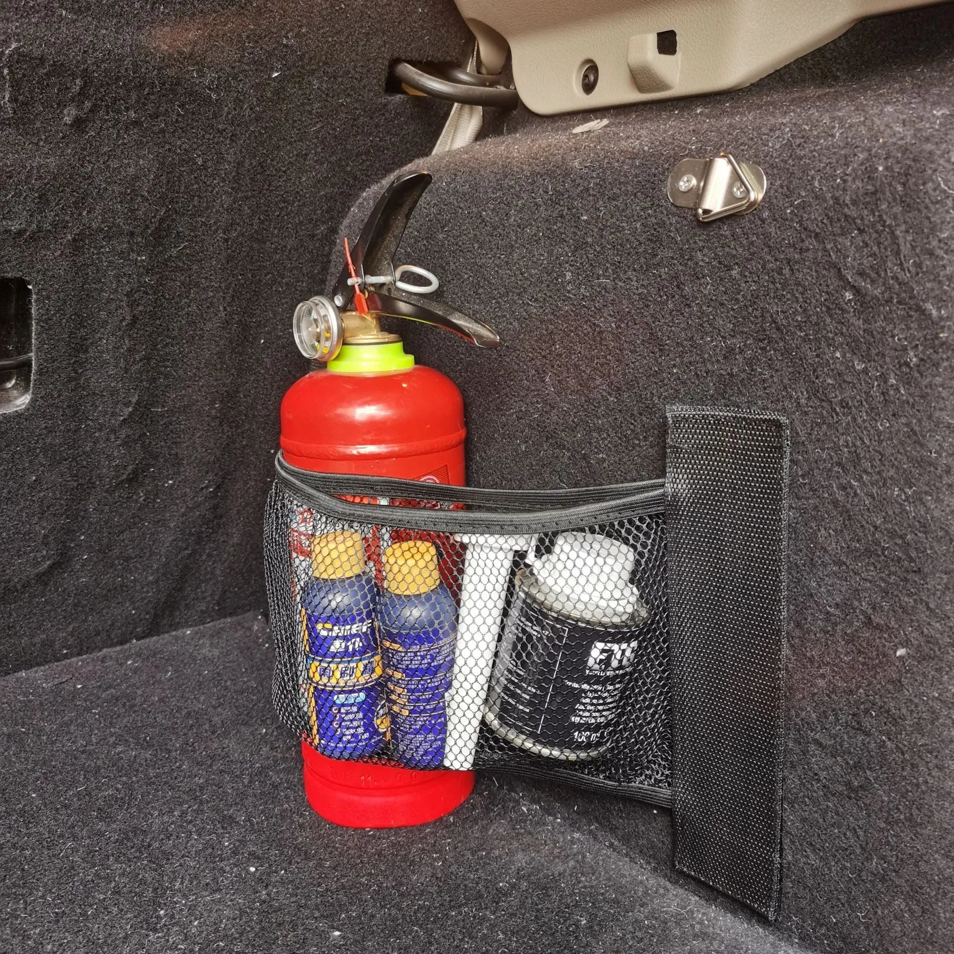 Black elastic polyester storage net stretched in a car boot, holding a water bottle and cloth.