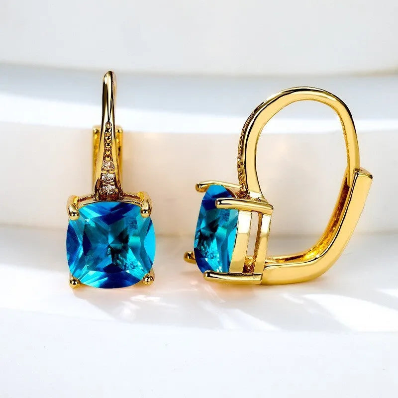 Geometric copper ear hook with round element and inlaid square zircon stone, shown in a golden colour.
