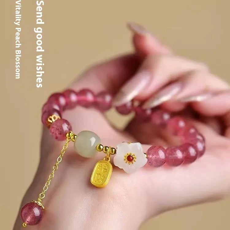 Handmade strawberry quartz crystal bracelet with Hetian jade peach blossom charm on a wrist.