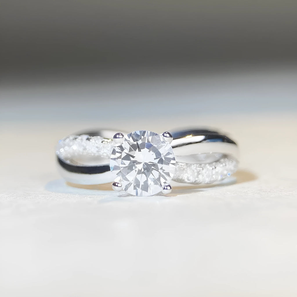 Women's silver ring with a 1 karat moissanite stone in a four-claw twisted arm setting, showing a geometric cross design.