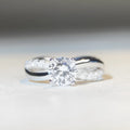 Women's silver ring with a 1 karat moissanite stone in a four-claw twisted arm setting, showing a geometric cross design.